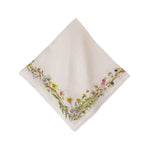 A beige linen napkin with a floral border featuring wildflowers, berries, and brambles.
