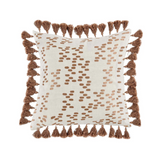 A square decorative pillow with light brown tassels and metallic embroidery on a light complexion background with dark accents.