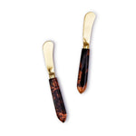 A pair of stainless steel butter knives with resin handles that have a tortoise swirl pattern.