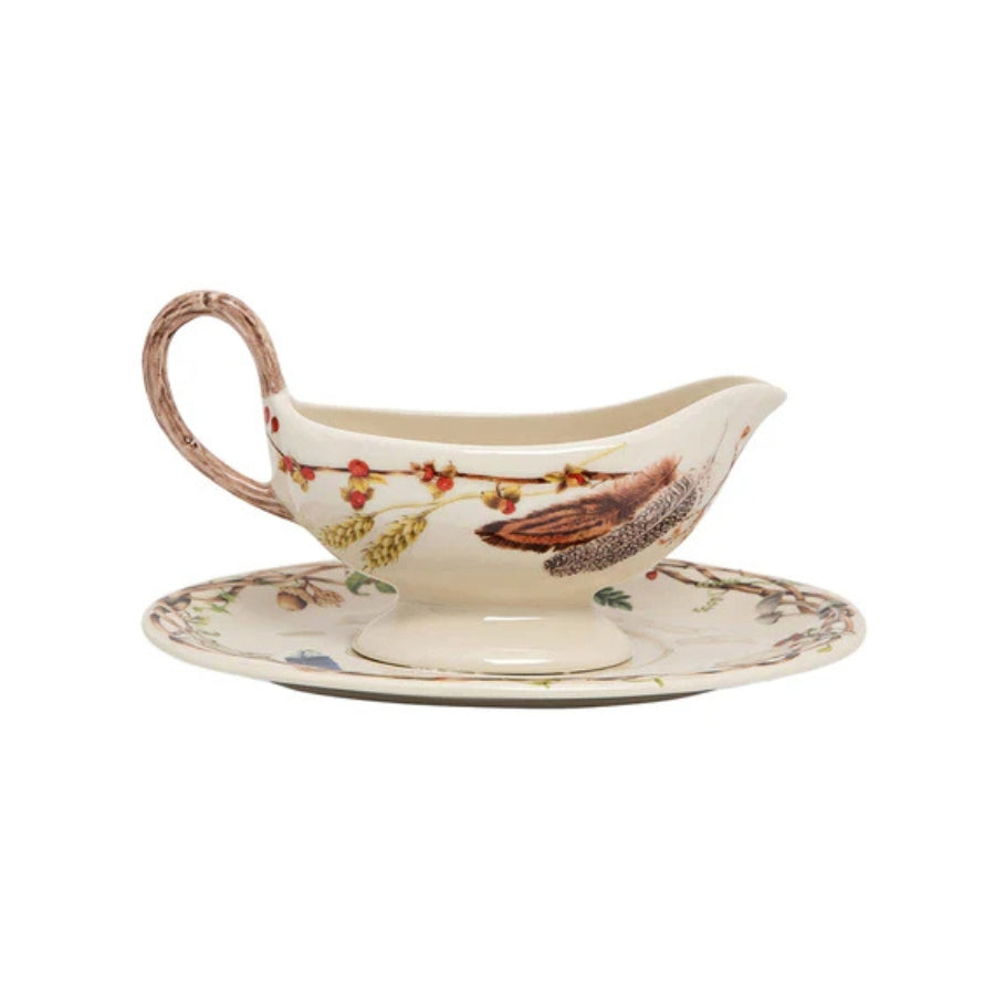 Ceramic gravy boat with decorative handle on a matching saucer against a white background