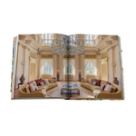 Open book showing a luxurious living room with beige sofas, a chandelier, and large windows.