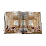 Open book showing a luxurious living room with beige sofas, a chandelier, and large windows.