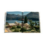 Open book showing a scenic view of a lakeside resort with mountains in the background.